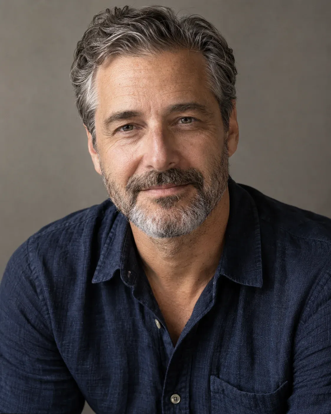 Adult man with salt-and-pepper hair in a textured navy shirt against a warm studio backdrop.